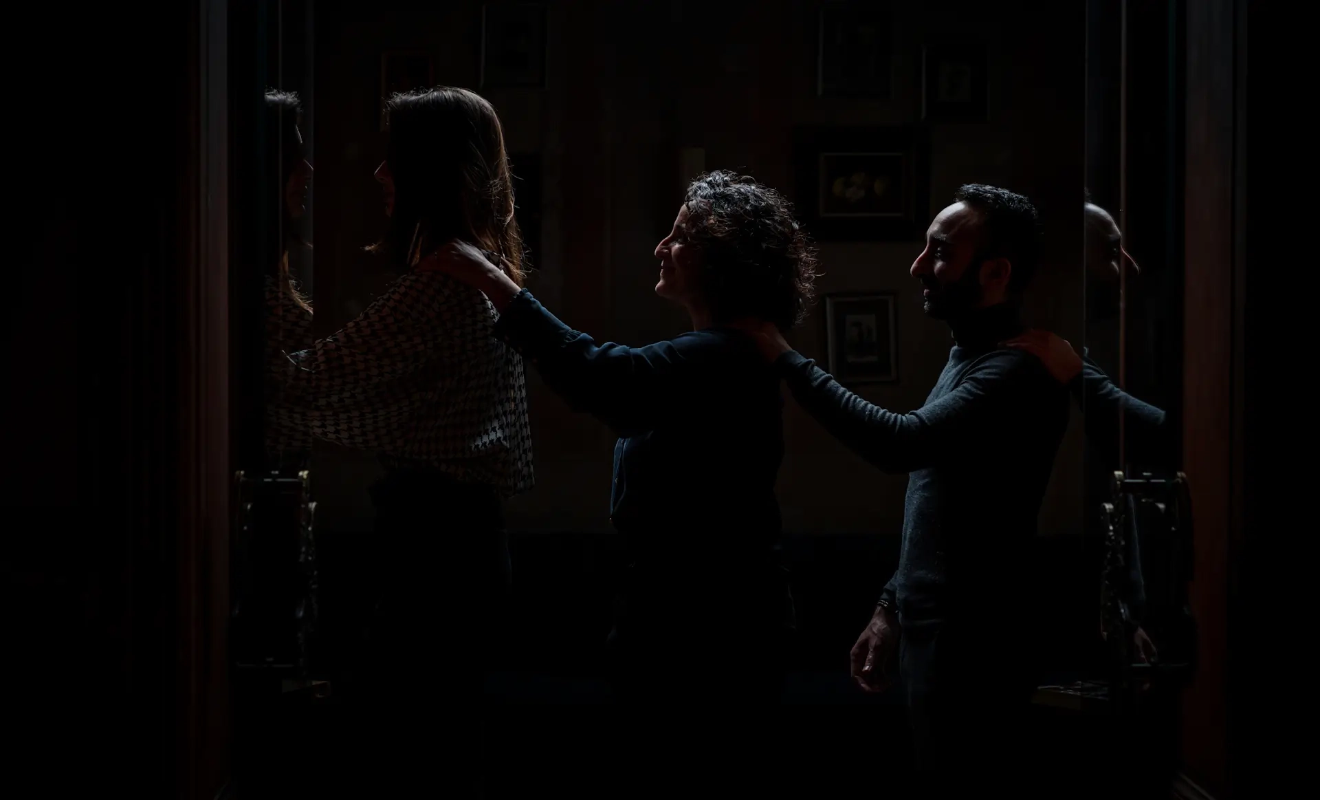 Trois personnes avancent en file indienne, une main posée sur l’épaule de la personne devant, dans une atmosphère sombre évoquant une expérience sensorielle dans le noir.